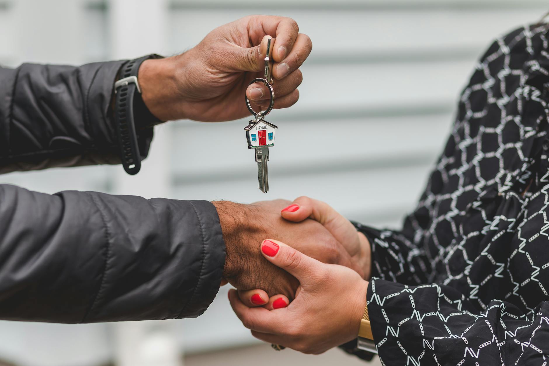 Handover of keys between two people with a handshake, symbolising the closing of a real estate deal.